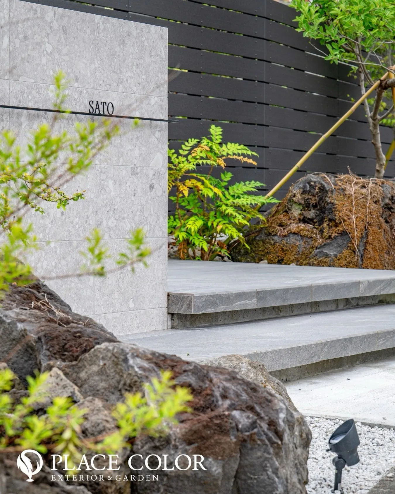 重厚感のある石景と瑞々しい植栽に、端正な門柱と黒の横ラインを...